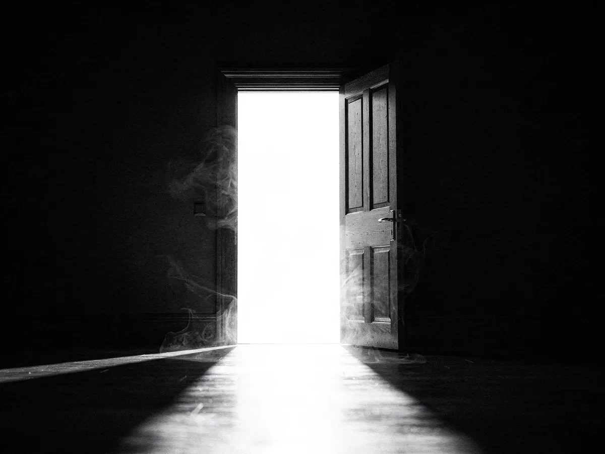 A door swung wide open in a dark room, bright light pouring through the doorway across the floor
