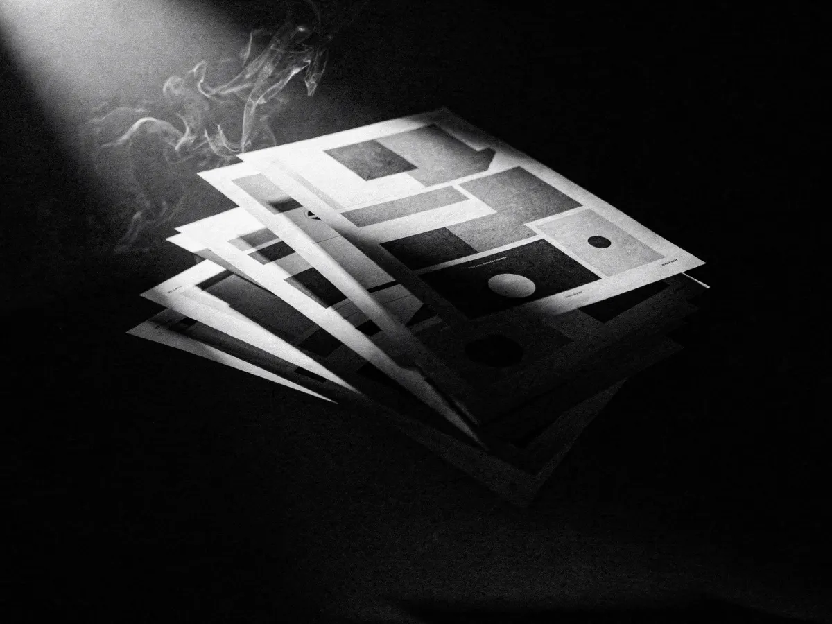 Printed page layouts fanned against a black void, one sheet caught in a hard raking light